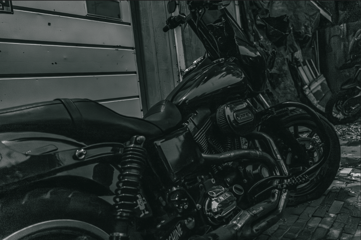 Black and white photo of a classic custom bobber motorcycle parked beside a rustic wooden building.