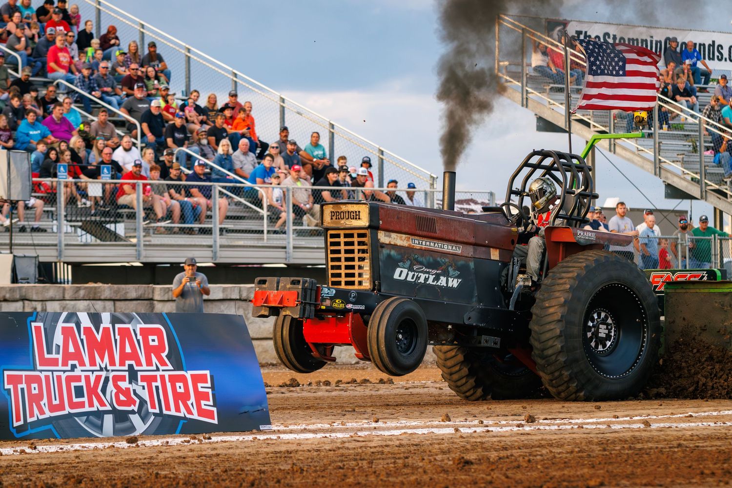 Modified tractor pulling competition with black smoke exhaust at a packed grandstand event.