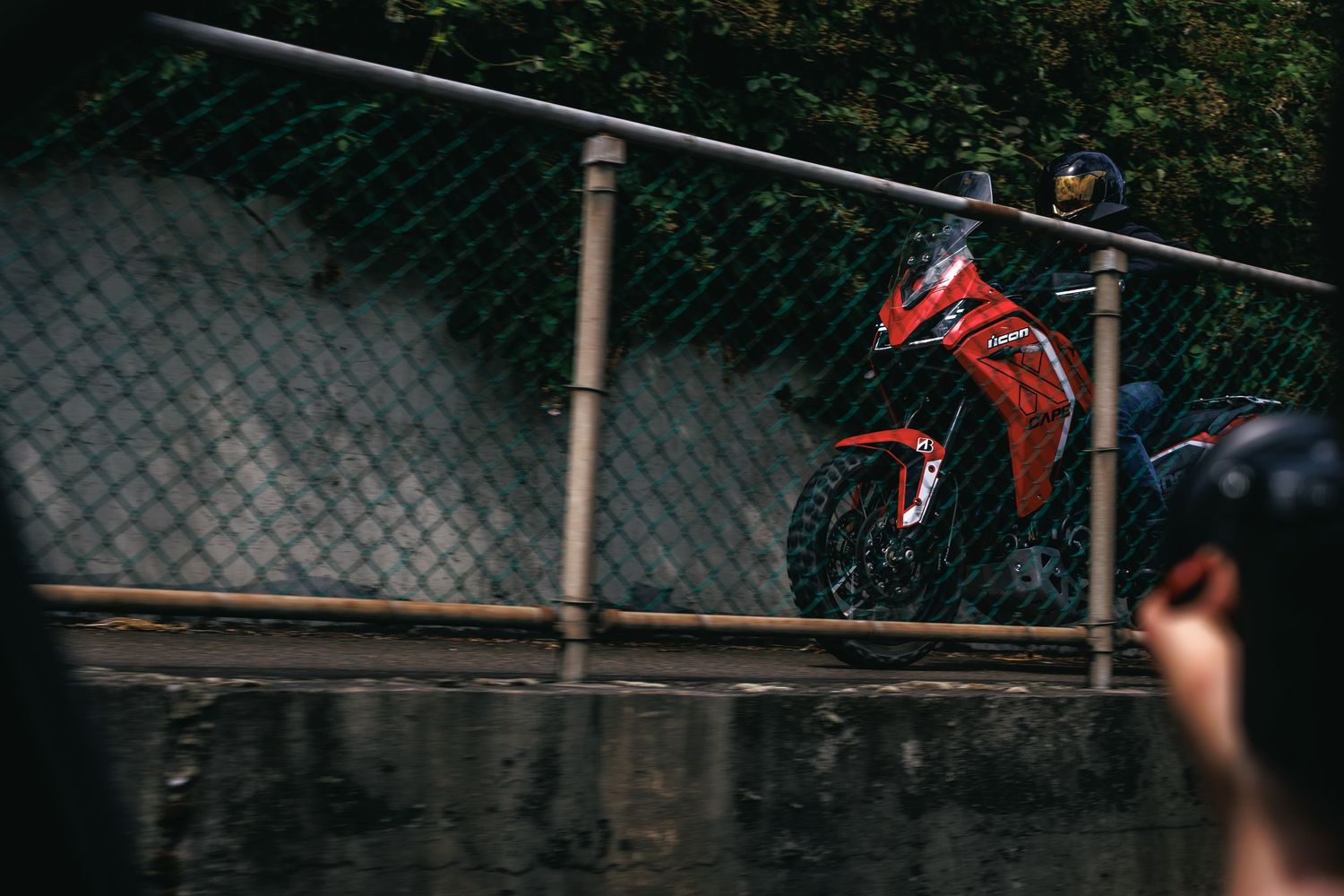 Red sport motorcycle parked behind a chain-link fence on a wet rainy day.