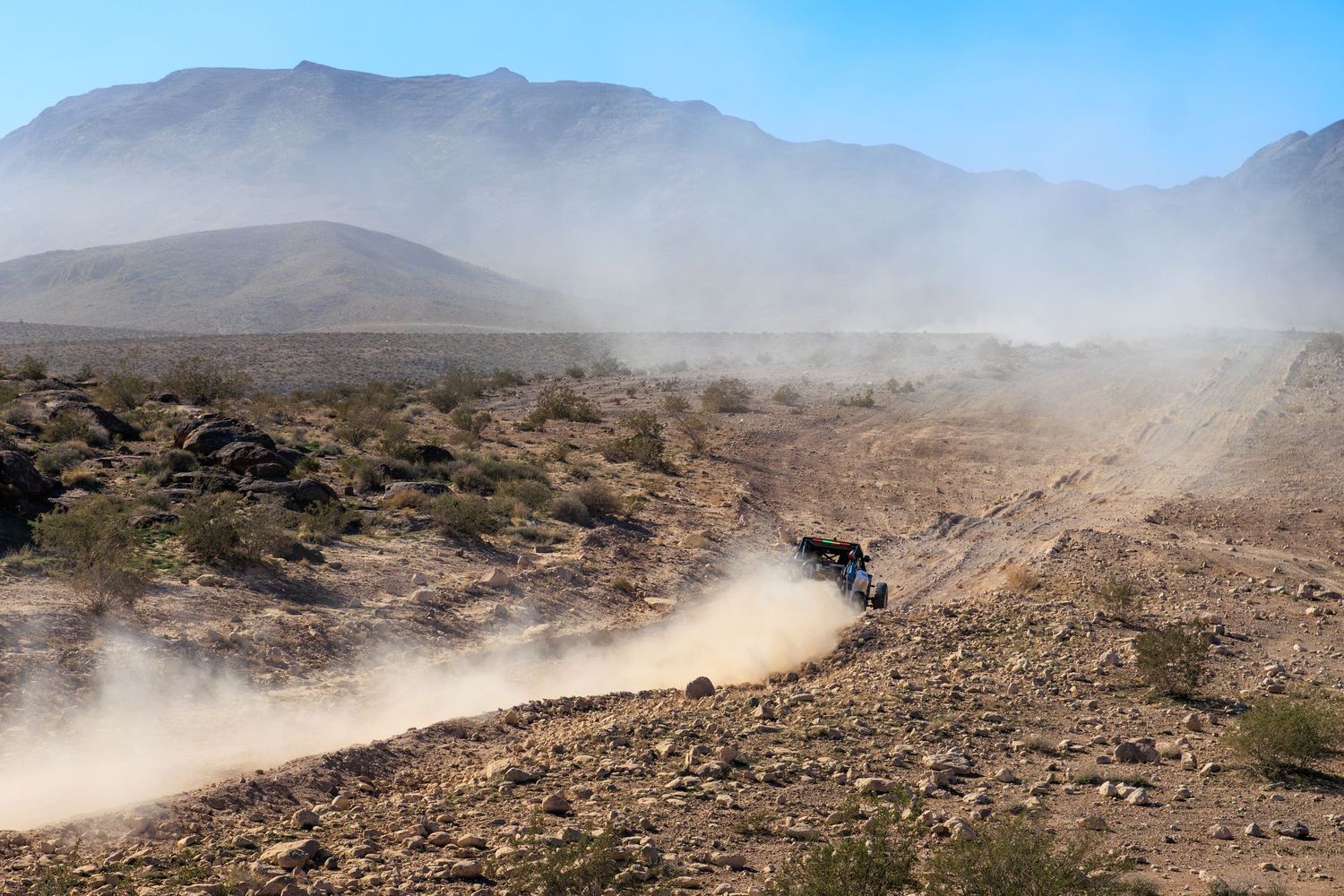 Off-road vehicle racing through dusty desert terrain with mountains in the background.