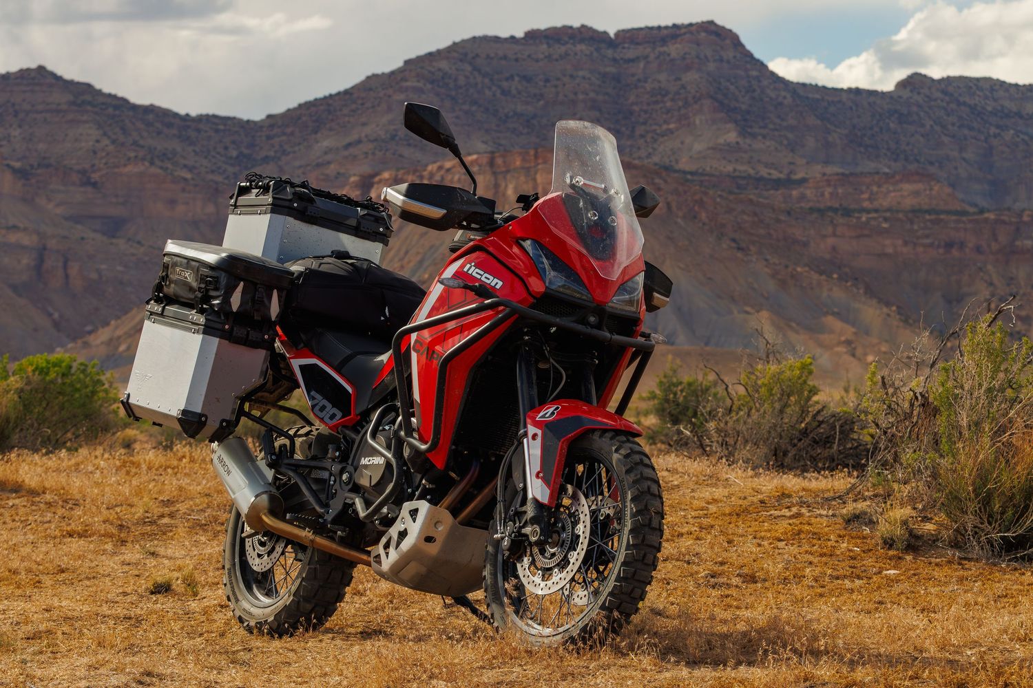 Red Honda adventure motorcycle with aluminum panniers parked in desert canyon landscape.