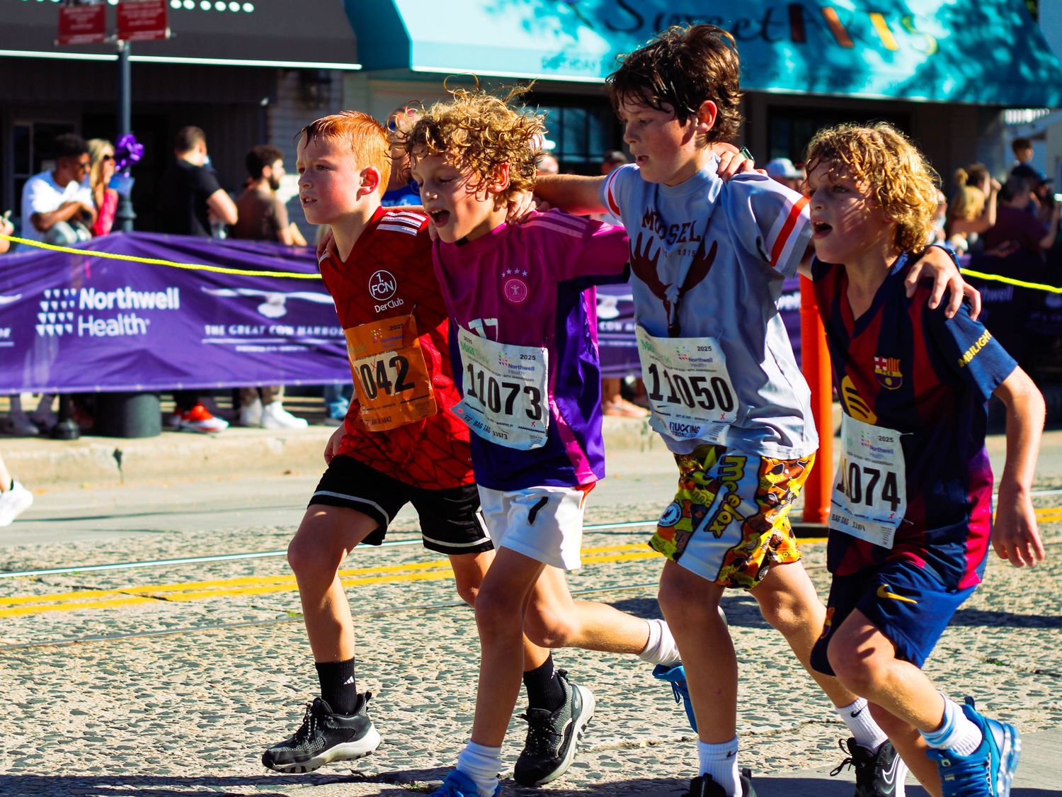Young runners help each other cross the finish line at the Cow Harbor Race