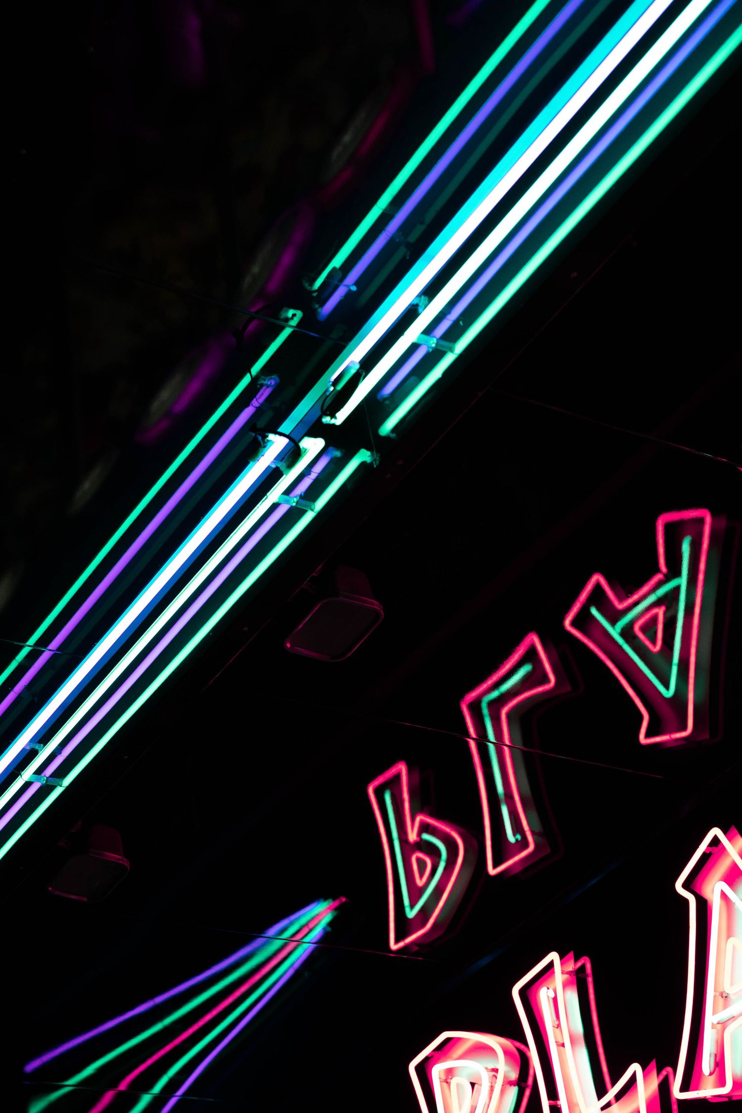 Vibrant neon signs glow in pink and teal against a dark night sky, creating a colorful urban nightlife display.