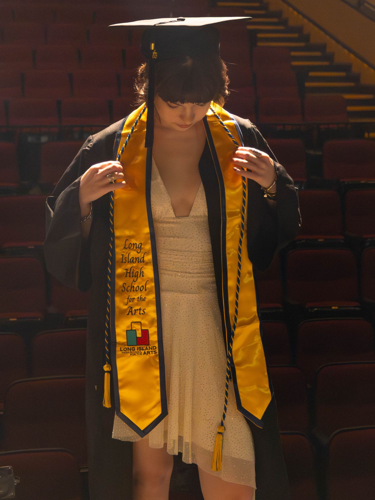 Graduate adjusting gold Long Island High School for the Arts stole over black gown.