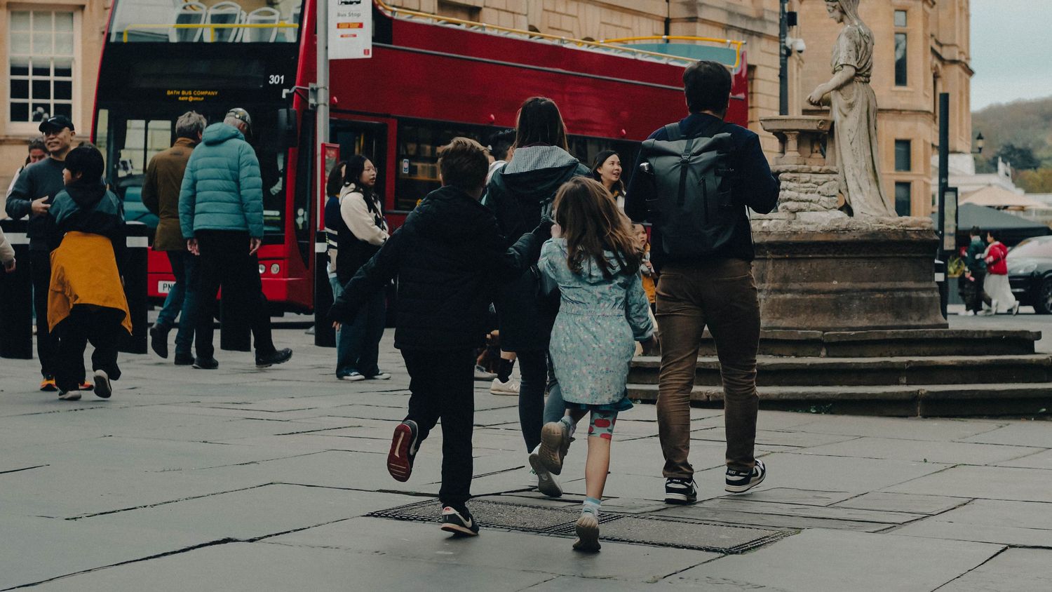 Group of people walking across a busy urban plaza with a red double-decker bus in the background.