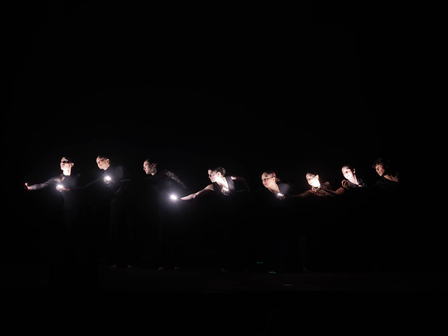 Performers hold bright lights in a line creating a striking visual effect on a dark stage.