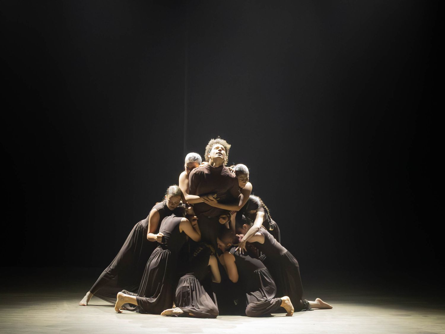 Dancers forming a human pyramid under a spotlight on a dark stage in a powerful performance.
