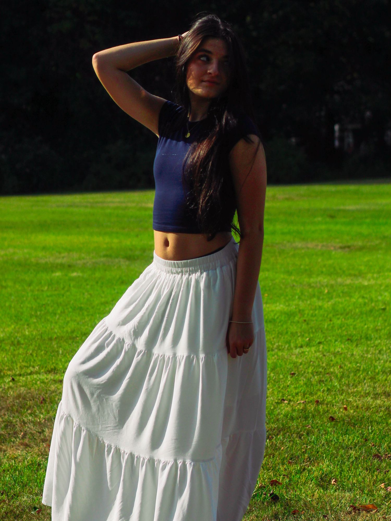 Woman wearing navy crop top and white tiered maxi skirt posing outdoors on sunny green grass.