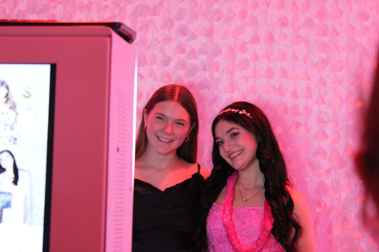 Two teenage girls posing together in a pink photo booth at a festive party event.