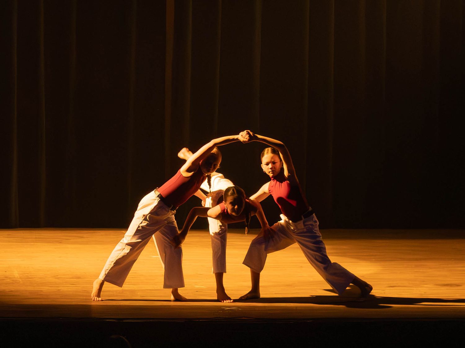 Three performers in red and white costumes strike a dynamic pose on a dimly lit stage during a dance performance.