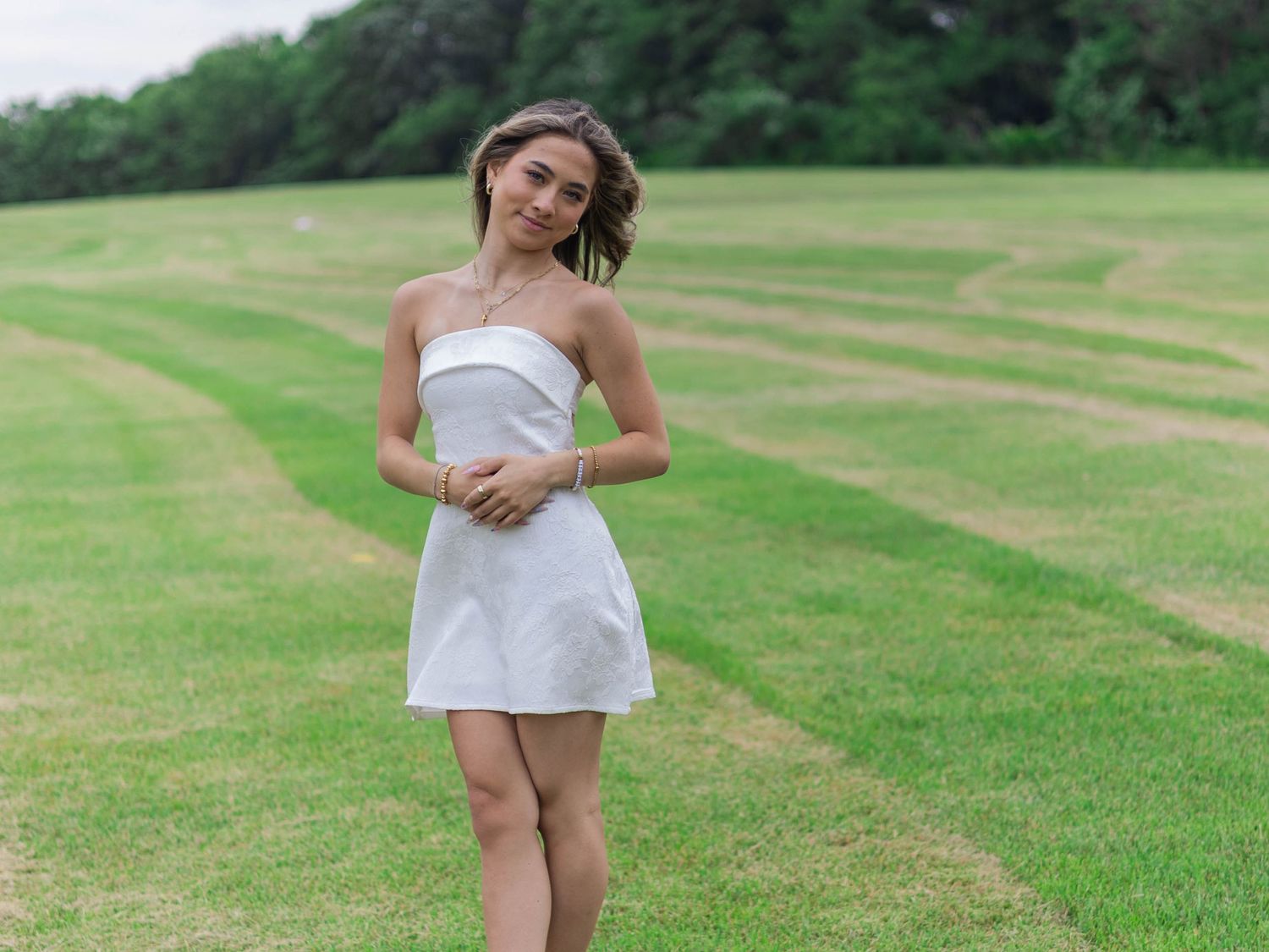 Young woman in white strapless mini dress poses gracefully on a lush green grass field.