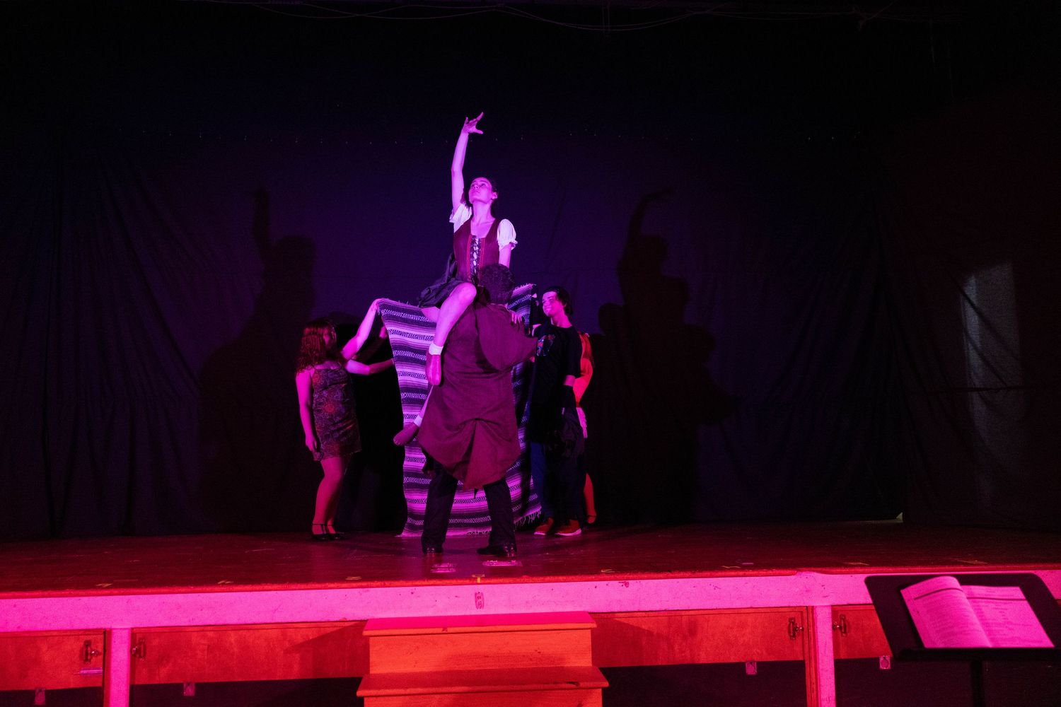 Performers on a dramatically lit stage with pink lighting during a theatrical dance production.