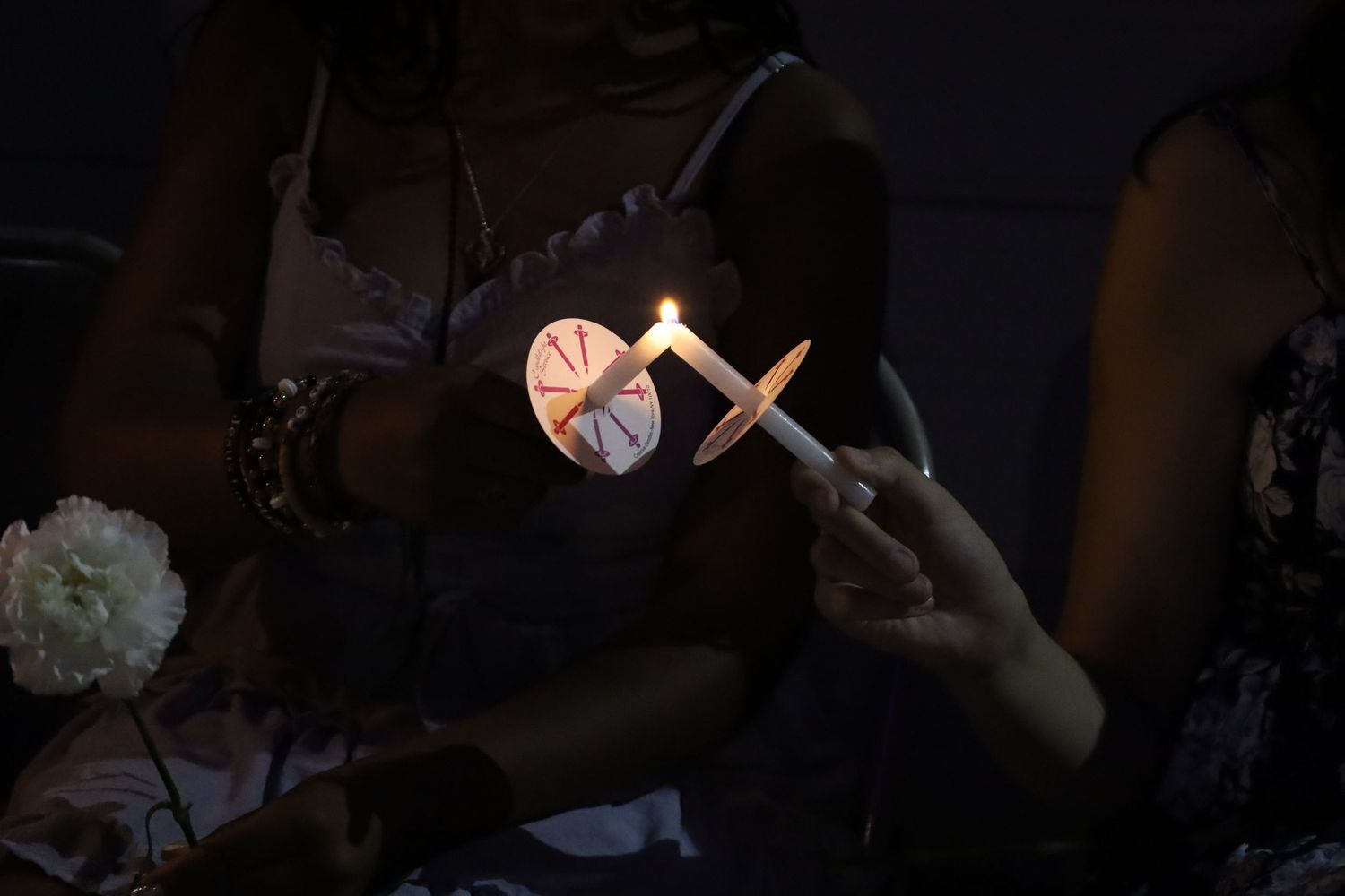 Hands holding a lit candle with a decorative heart-shaped holder in a dark ceremonial setting.