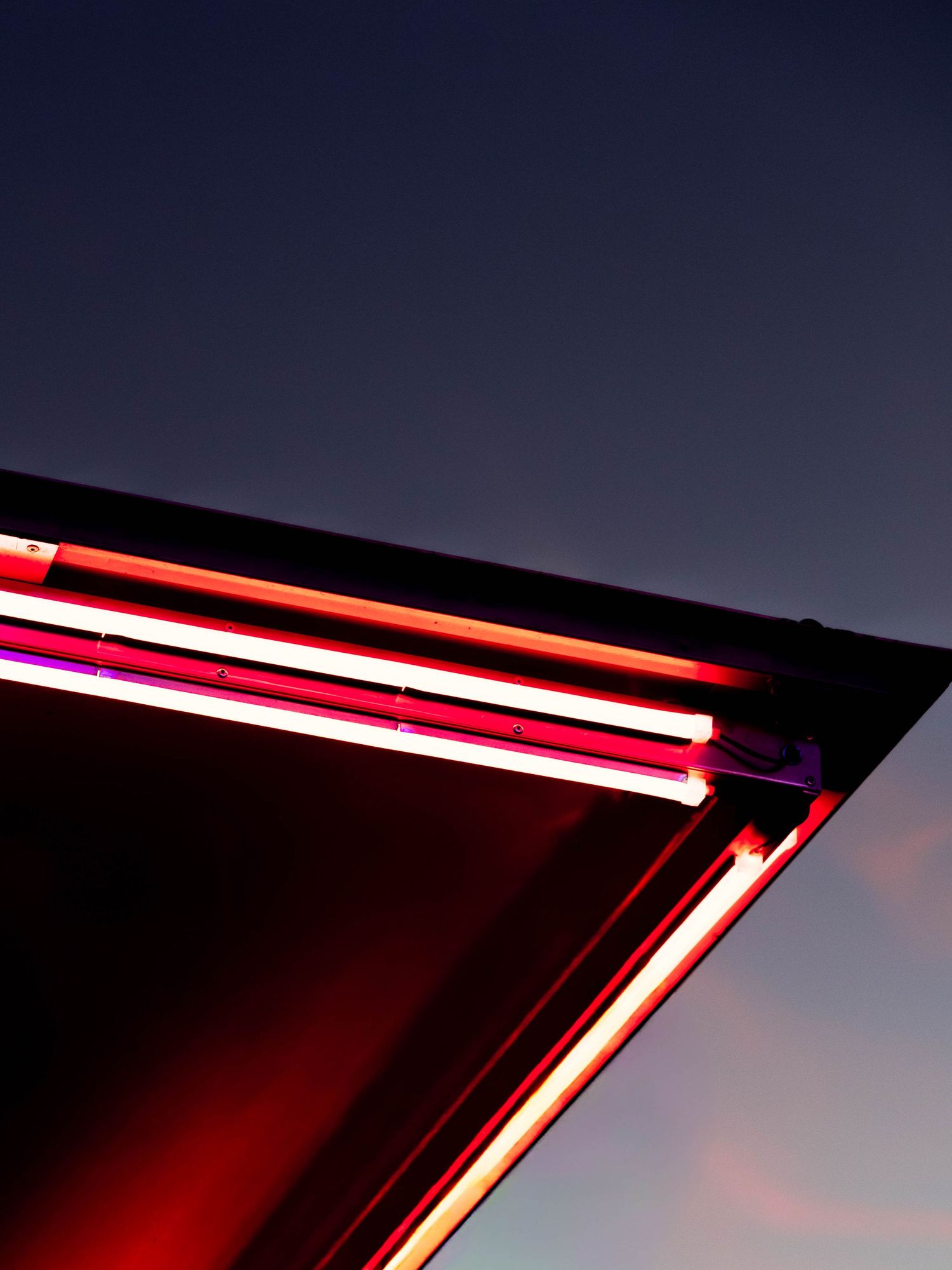 Vibrant red and pink neon lights glow on a rooftop edge against a dramatic dusk sky.