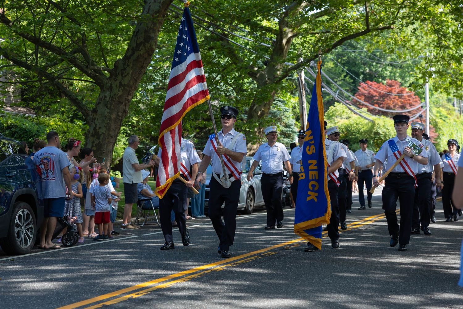 Honor guard marches with American flag and Land Neck banner during a sunny community parade.