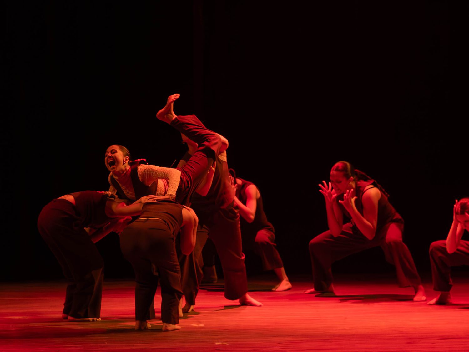 Dancers perform a dramatic contemporary dance piece under red stage lighting.