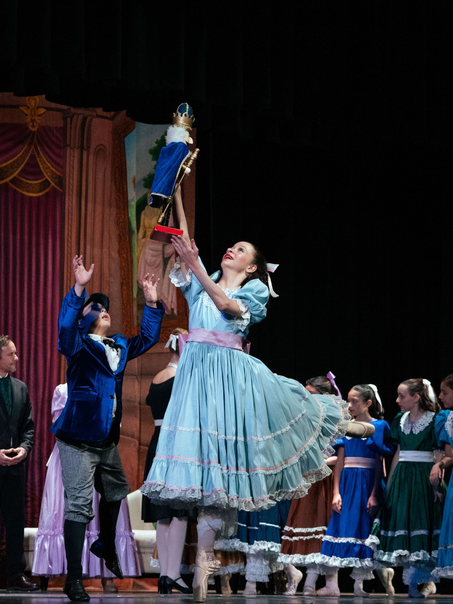 Ballet dancer in blue dress holds Nutcracker aloft on stage during a festive Nutcracker ballet performance.