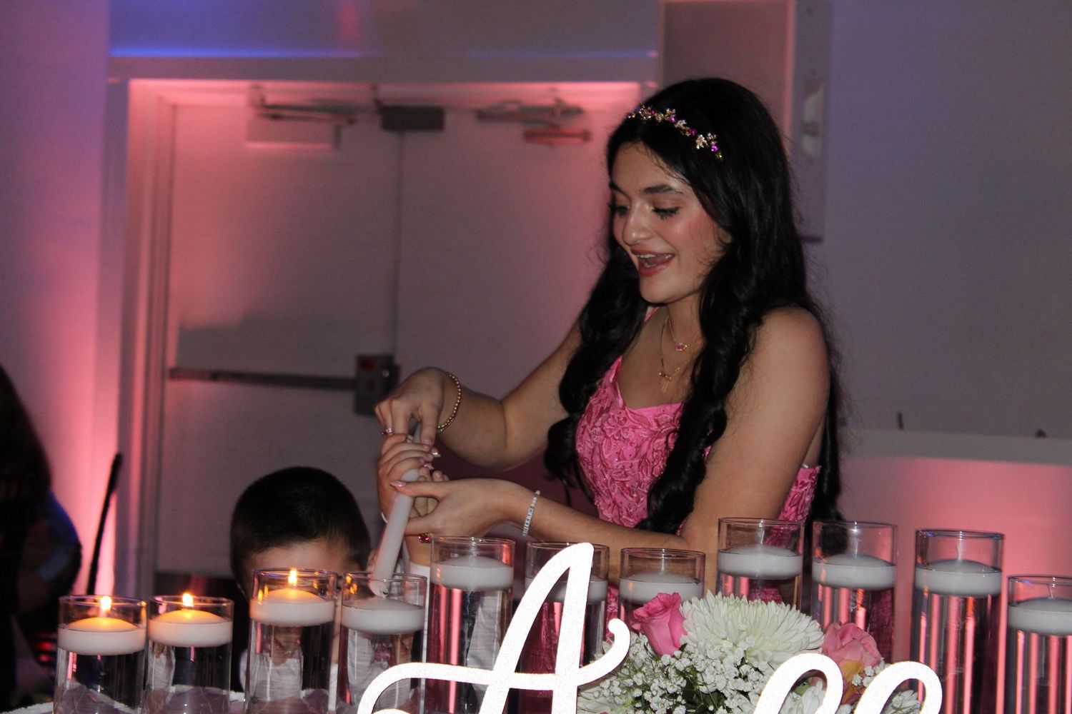 Young woman in pink quinceañera gown lighting candles at her elegant birthday celebration.