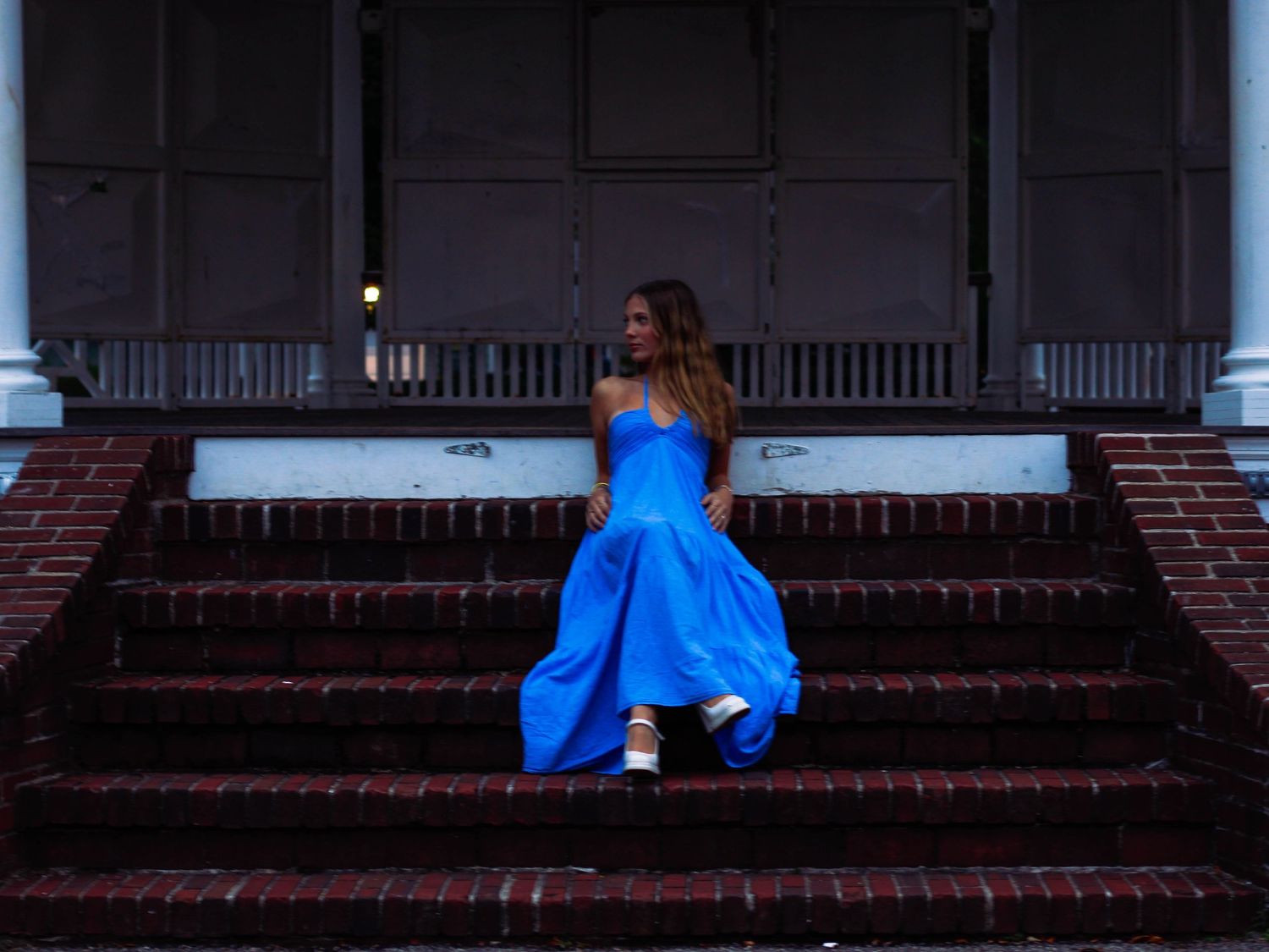 Woman in a strapless blue ball gown sitting on brick steps of a historic building.