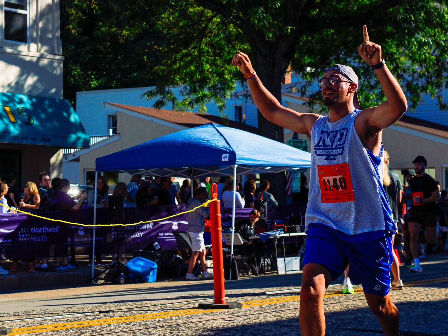 Jubilant male runner celebrates crossing the finish line at an outdoor road race on a sunny day.