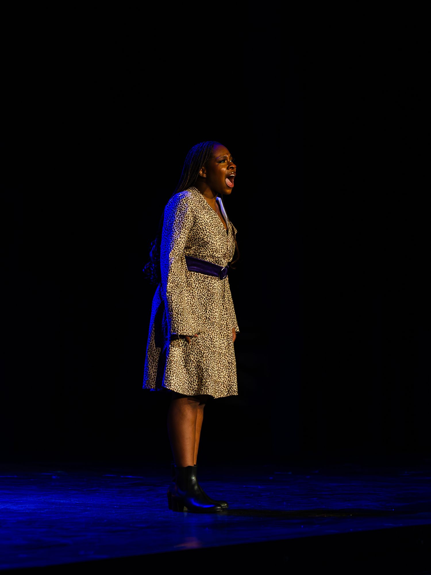 A woman in a floral dress performs solo on a dimly lit stage under a spotlight.