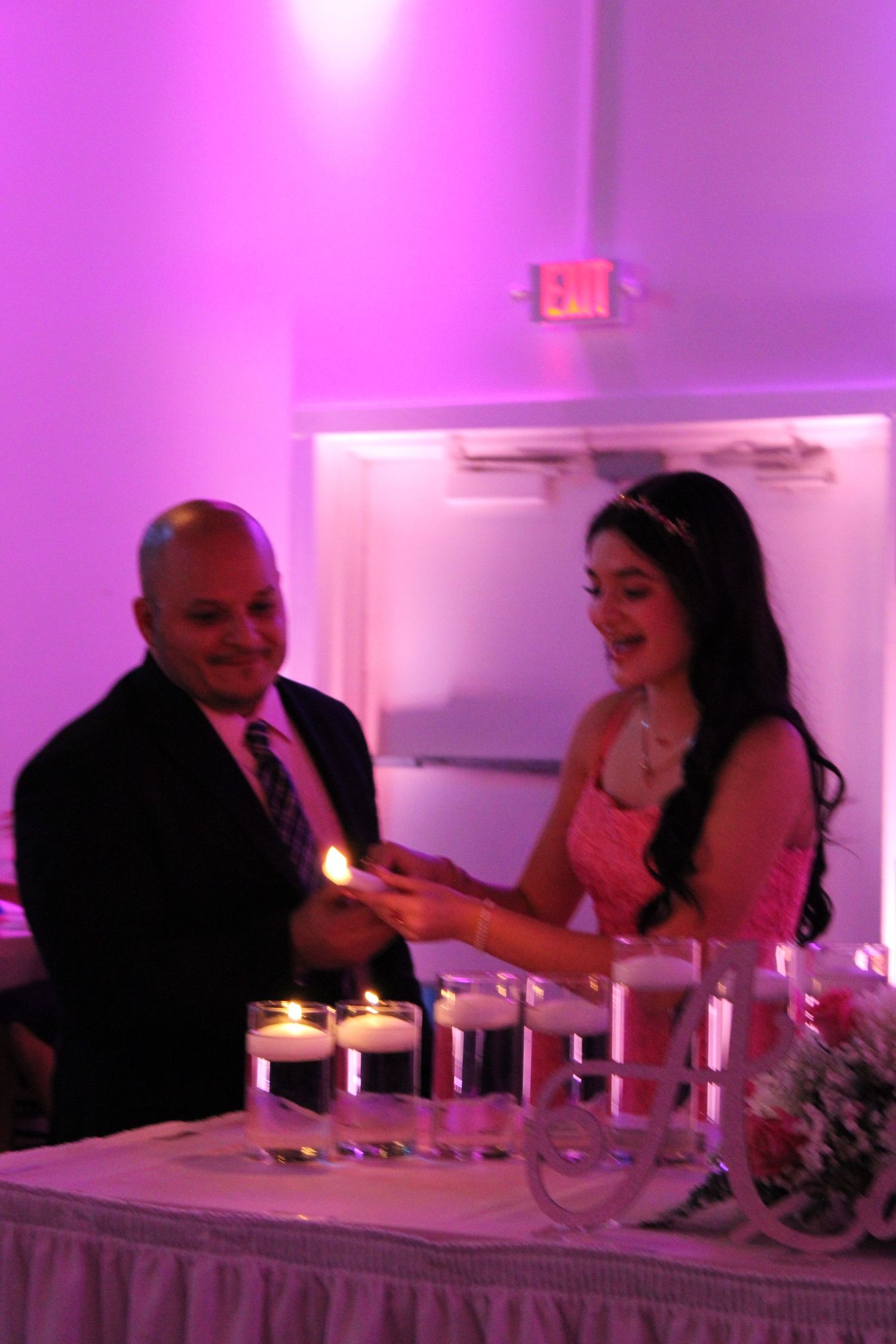 Man and young woman in pink dress lighting candles together at a quinceañera celebration.