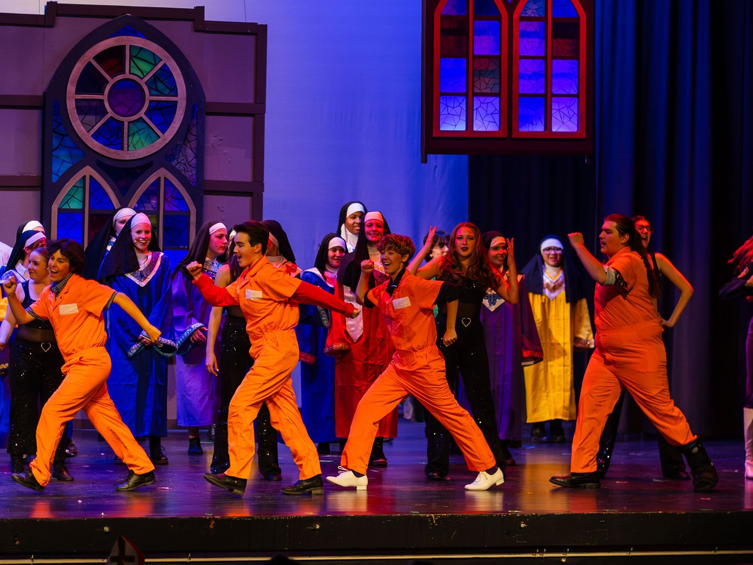 Performers in orange jumpsuits dance energetically on stage during a Sister Act musical production.
