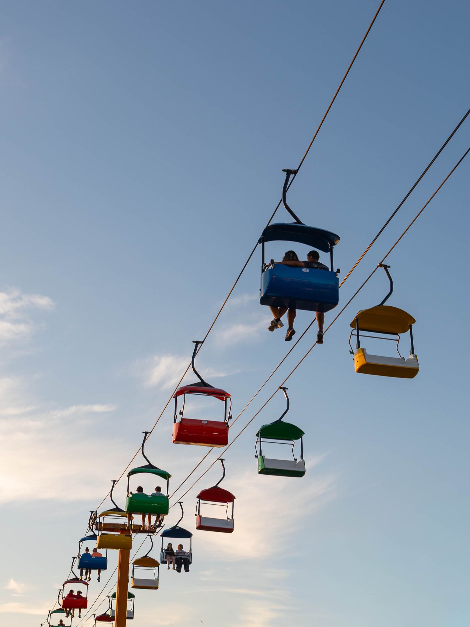 Colorful ski lift chairs carrying passengers against a blue sky at an amusement park or state fair.