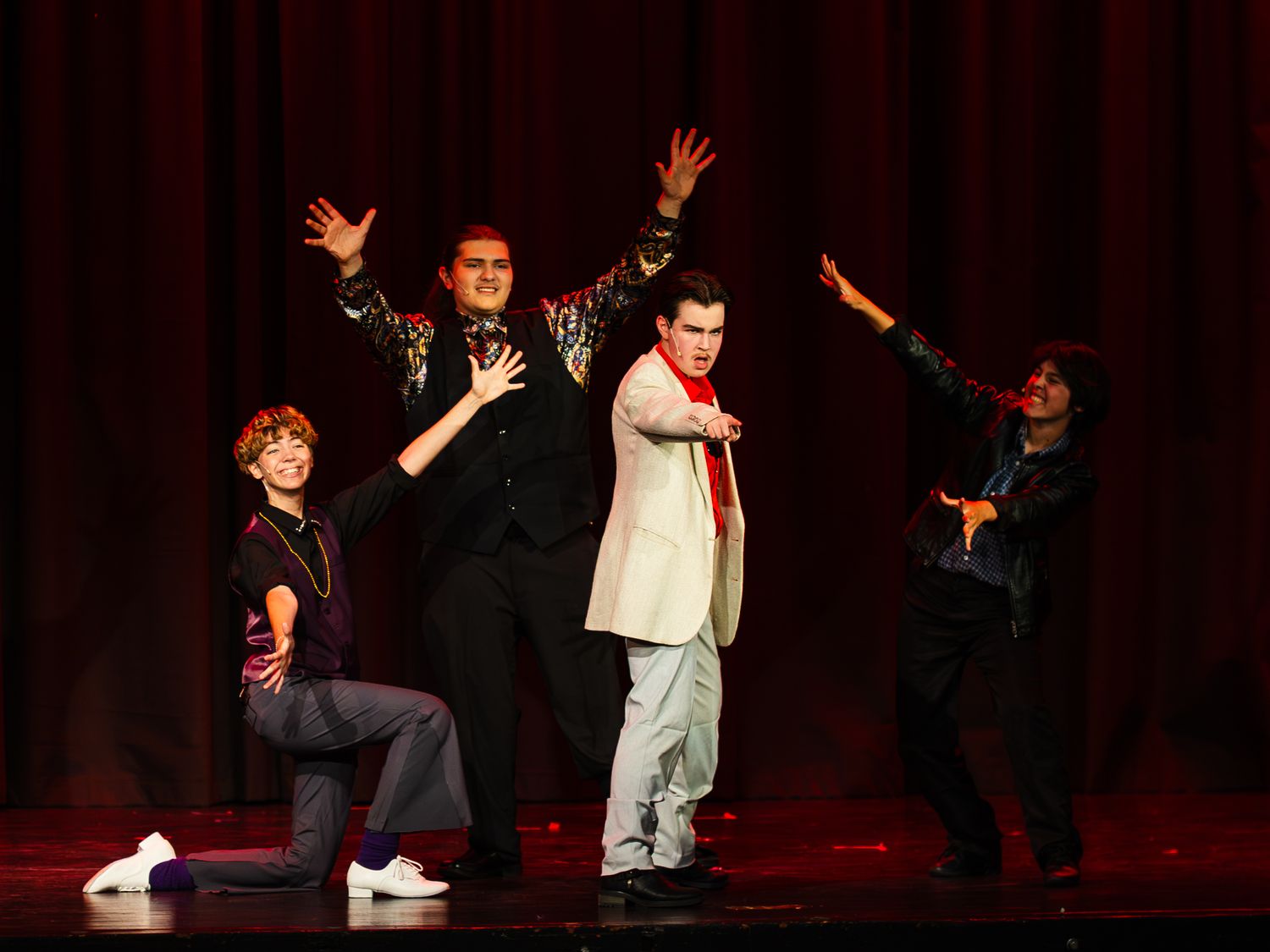 Four performers take a bow on stage in front of a red curtain during a theatrical production.