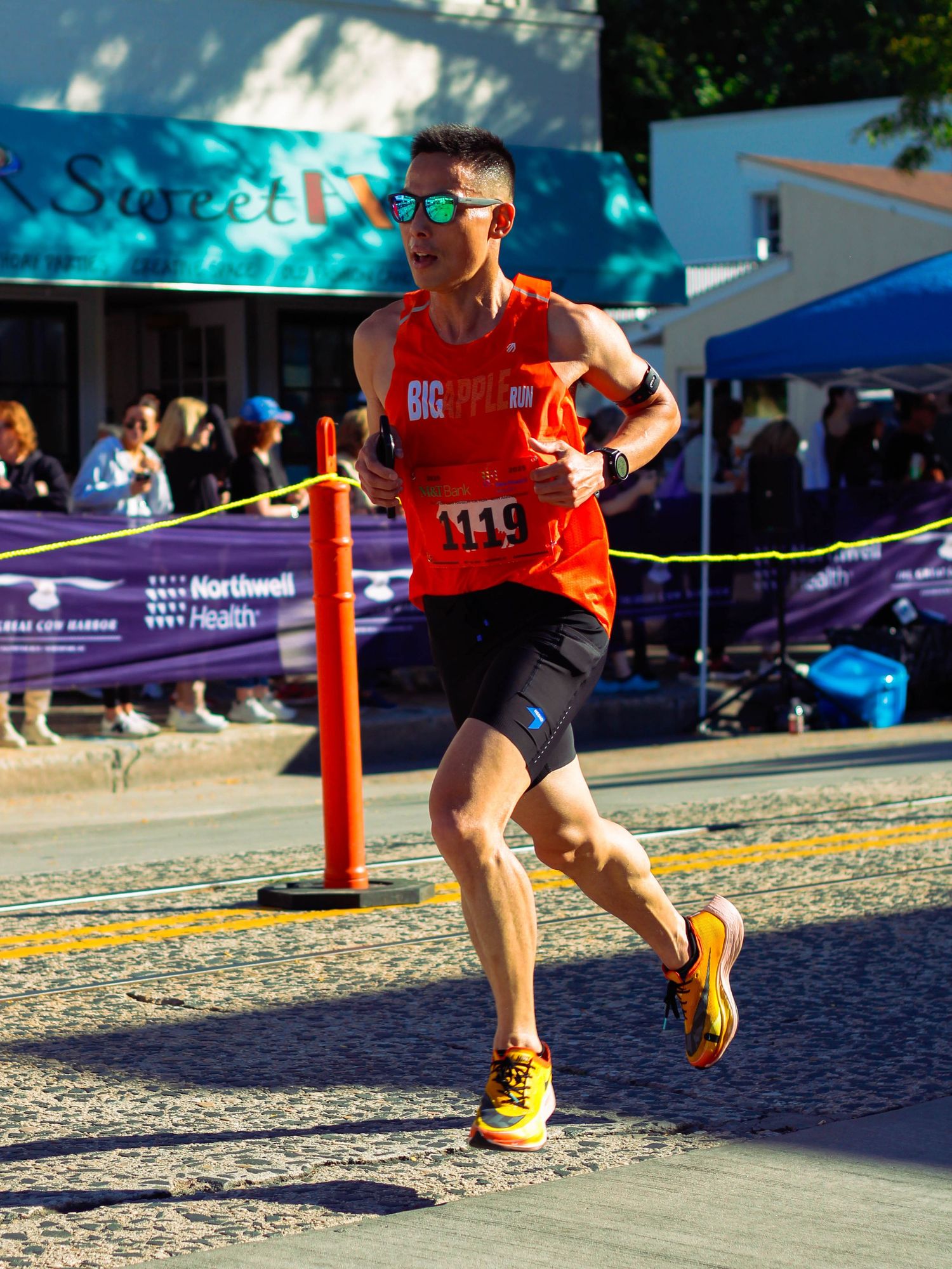 Male runner wearing bib number 1119 crosses the finish line at an outdoor road race event.