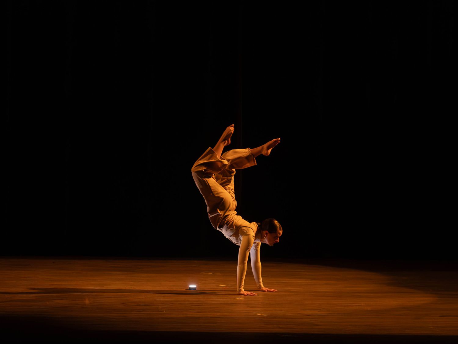 Dancer performing a handstand balance on stage with dramatic lighting against a dark background.