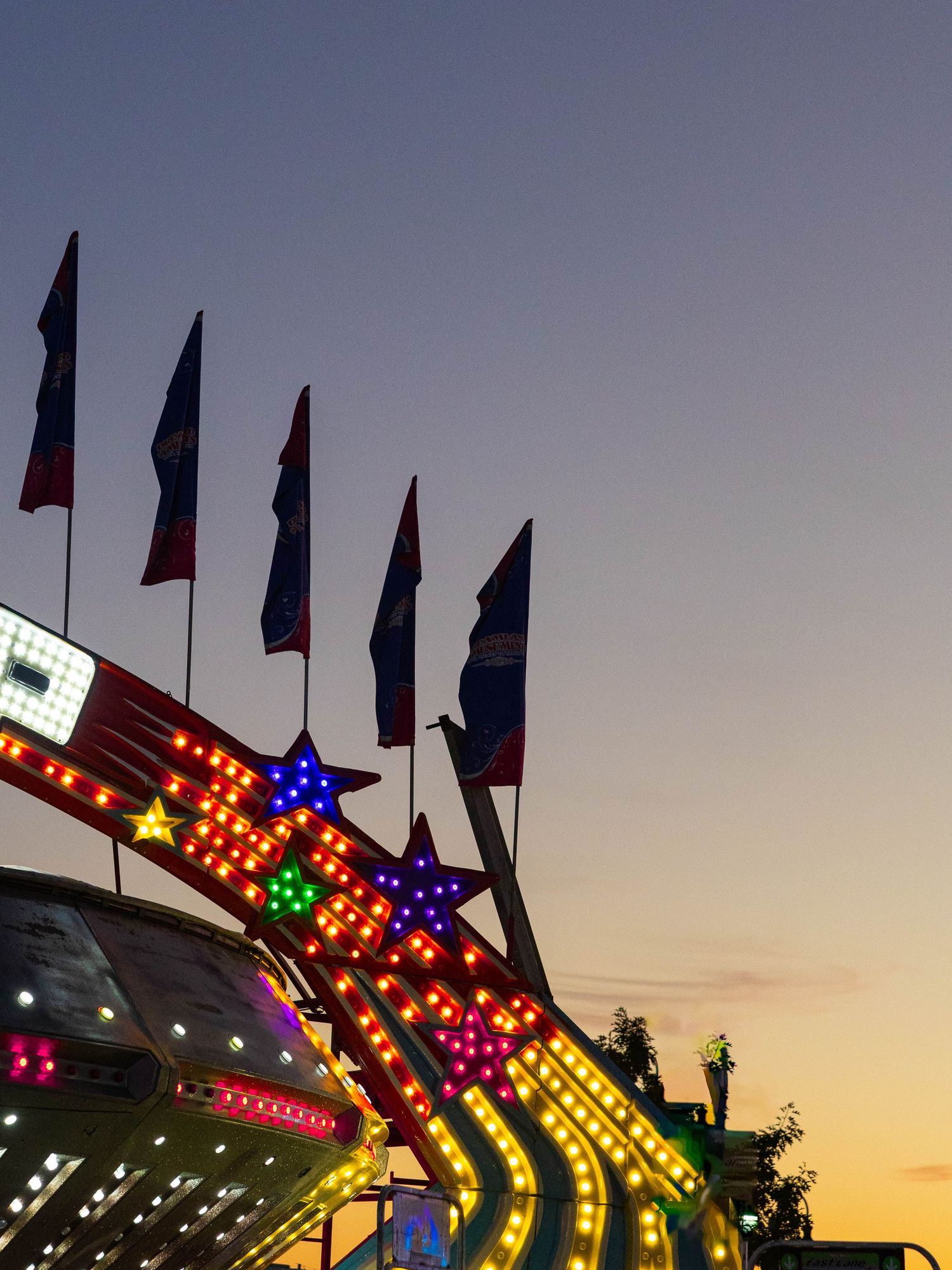 Colorful carnival ride lit up with star-shaped lights and flags against a twilight sky at a fairground.