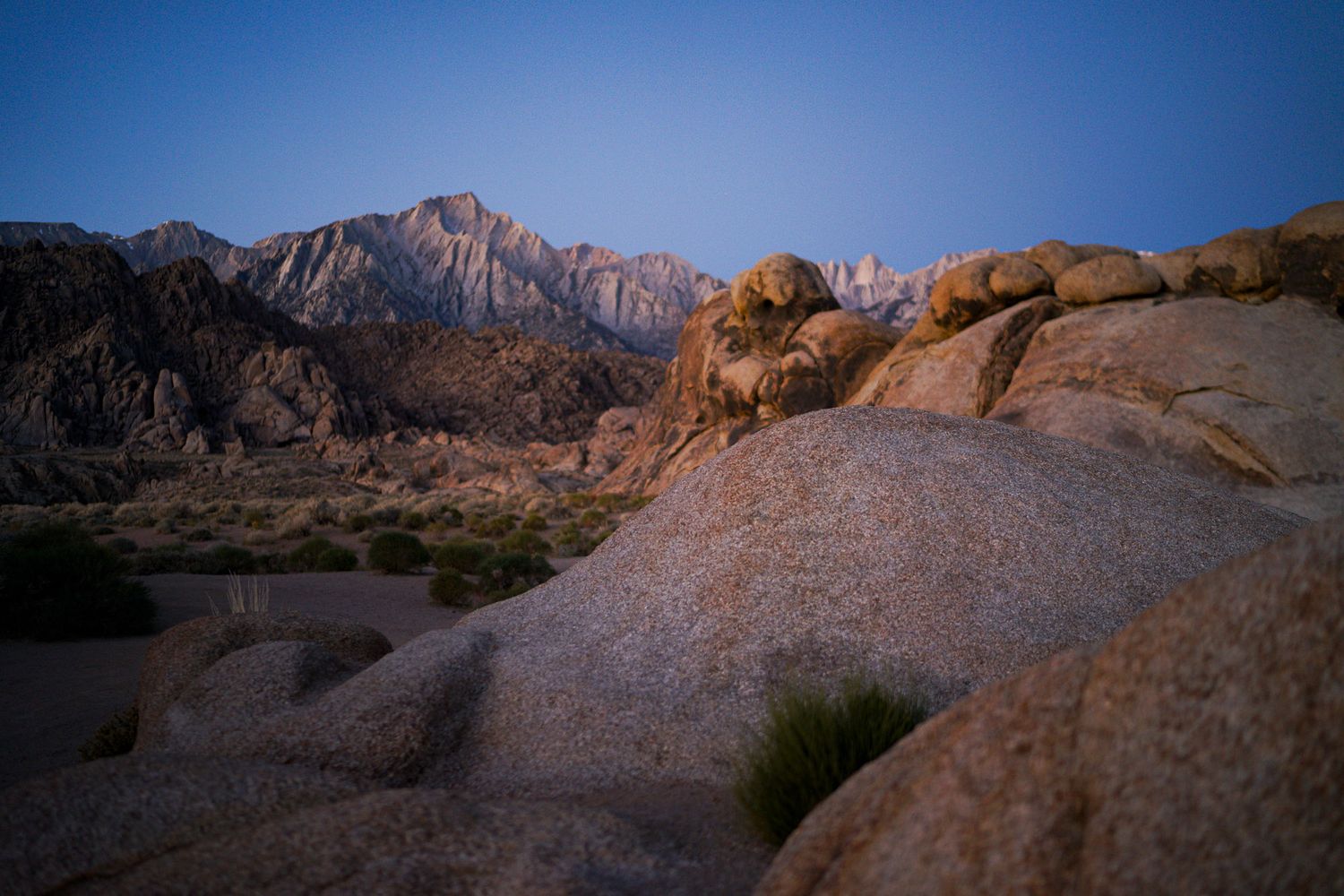 Dramatic granite boulders at Alabama Hills with Sierra Nevada mountains illuminated by golden sunset light.