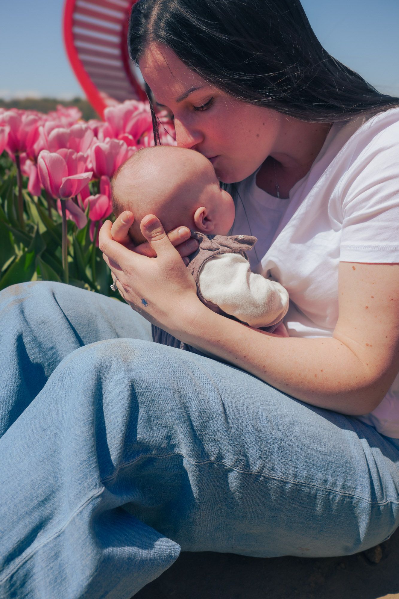 Mother kissing newborn baby in arms surrounded by pink tulips.
