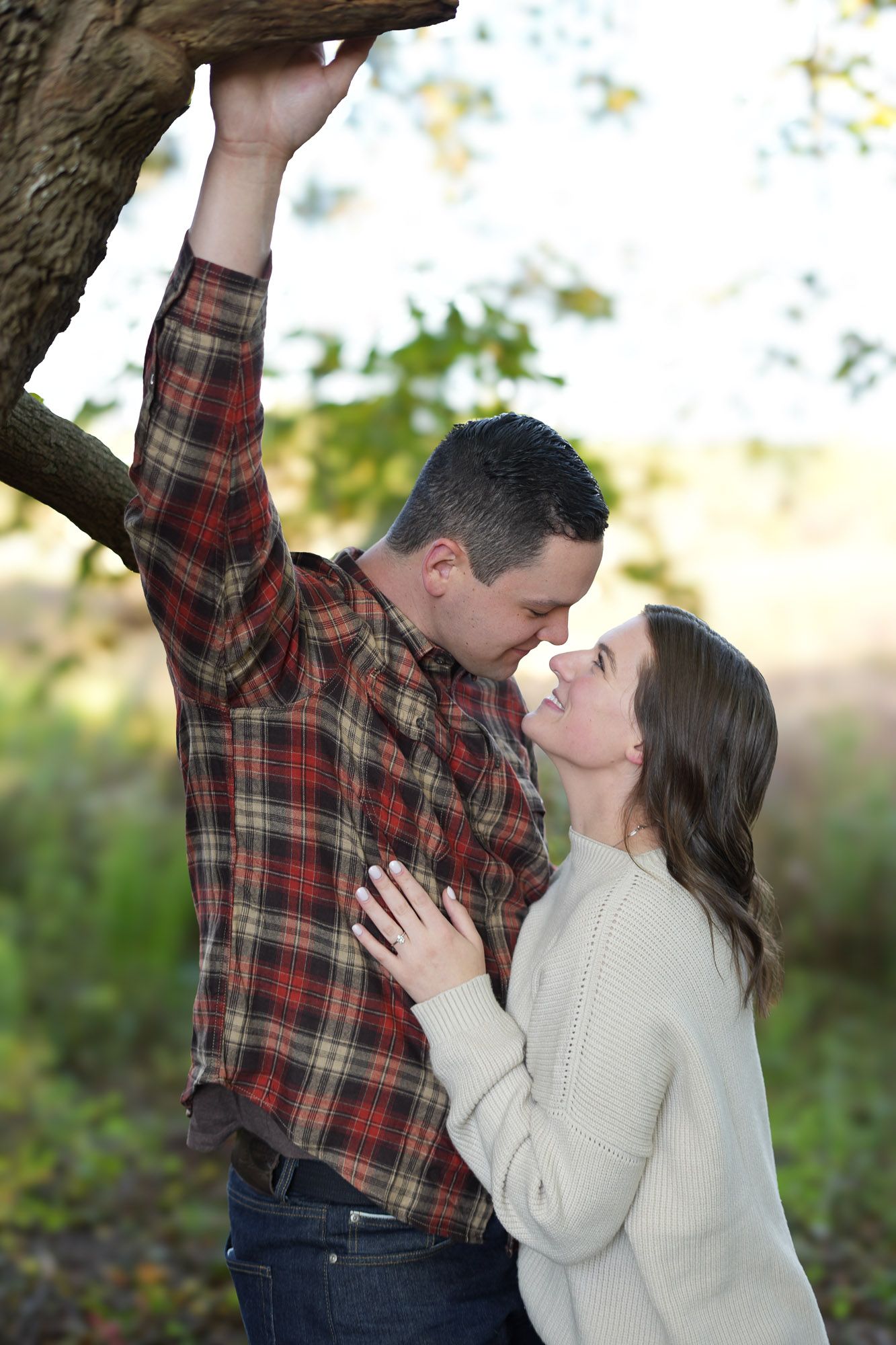 Romantic couple almost kissing under a tree branch in a bright outdoor natural setting.
