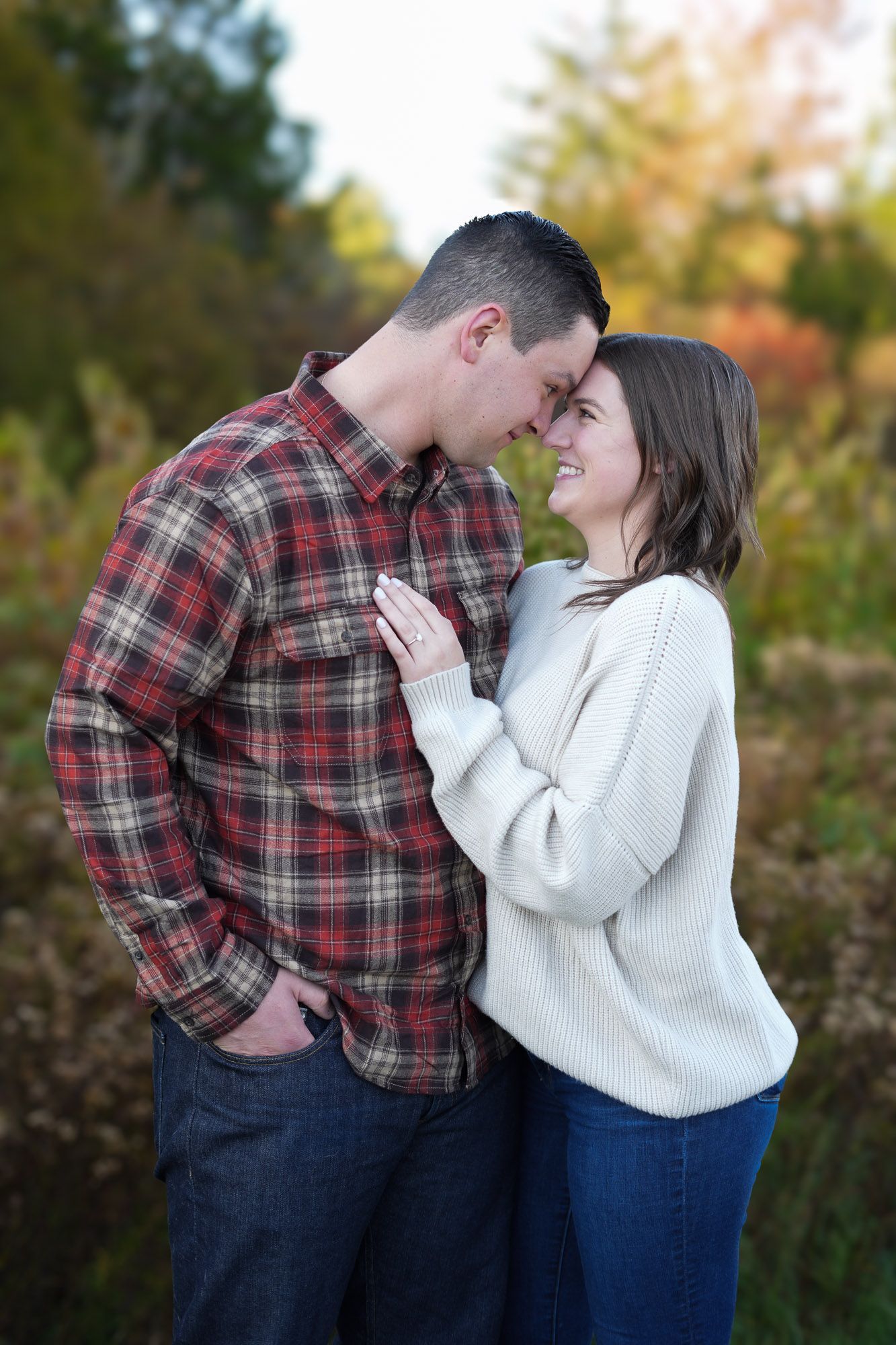Happy couple touching foreheads and smiling at each other in a colorful autumn outdoor setting.