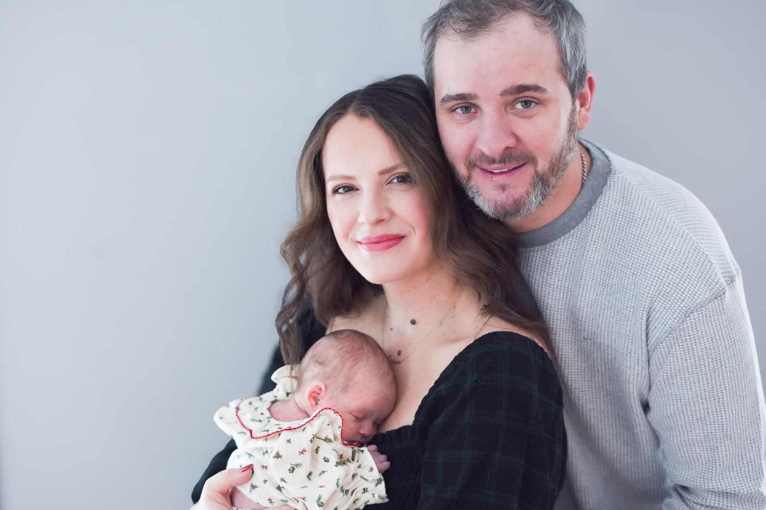 Smiling couple posing together holding their sleeping newborn baby.