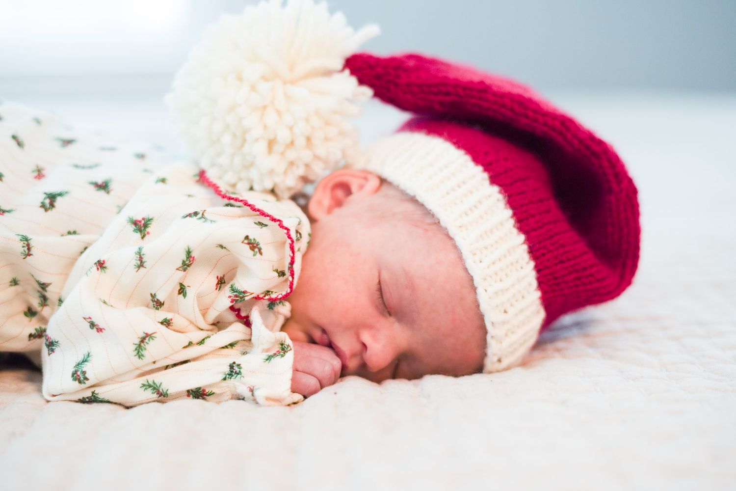 Sleeping newborn baby wearing a red and white Santa hat on a soft white blanket.