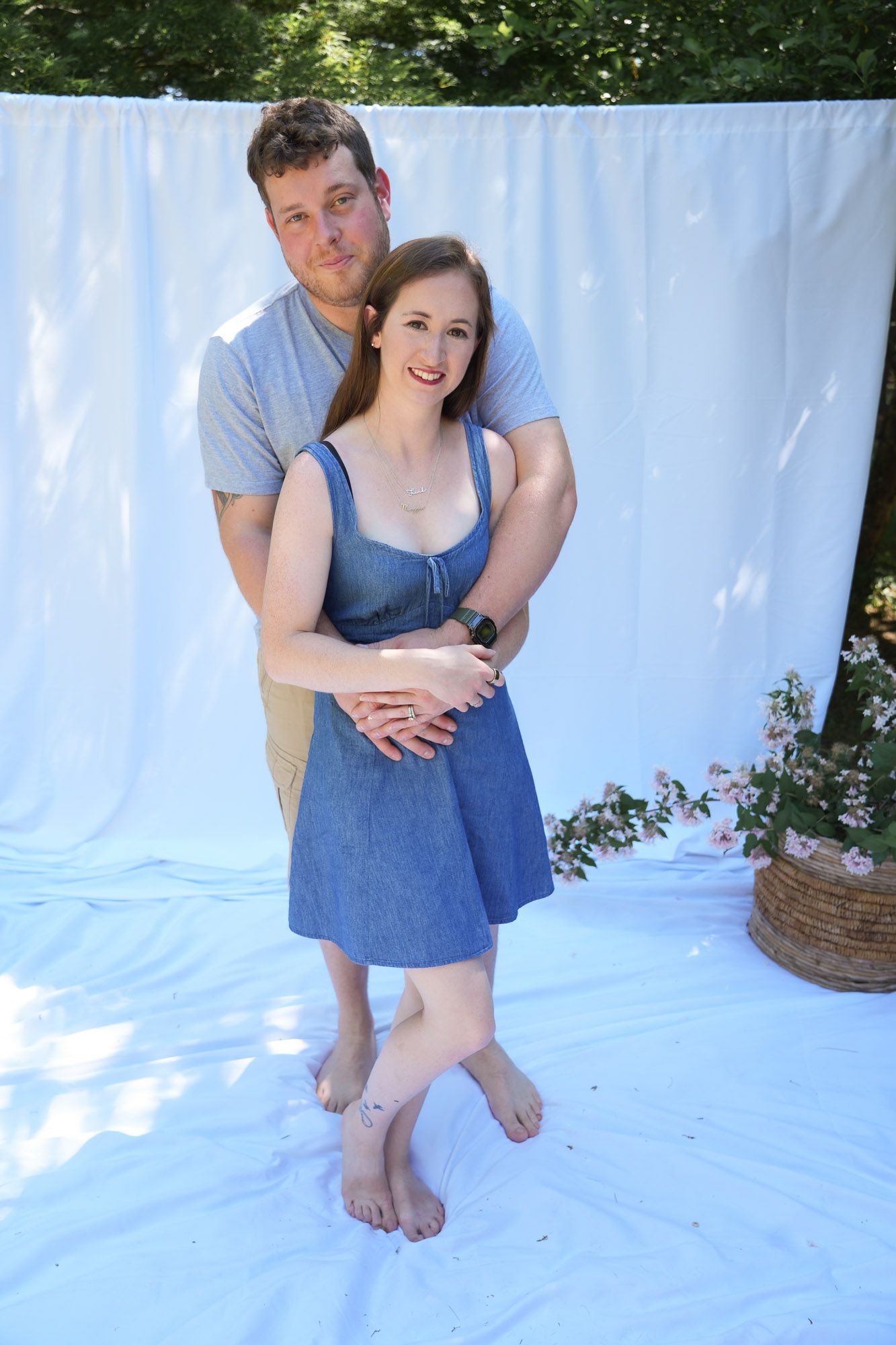 Smiling couple posing together outdoors with man embracing woman in blue dress.