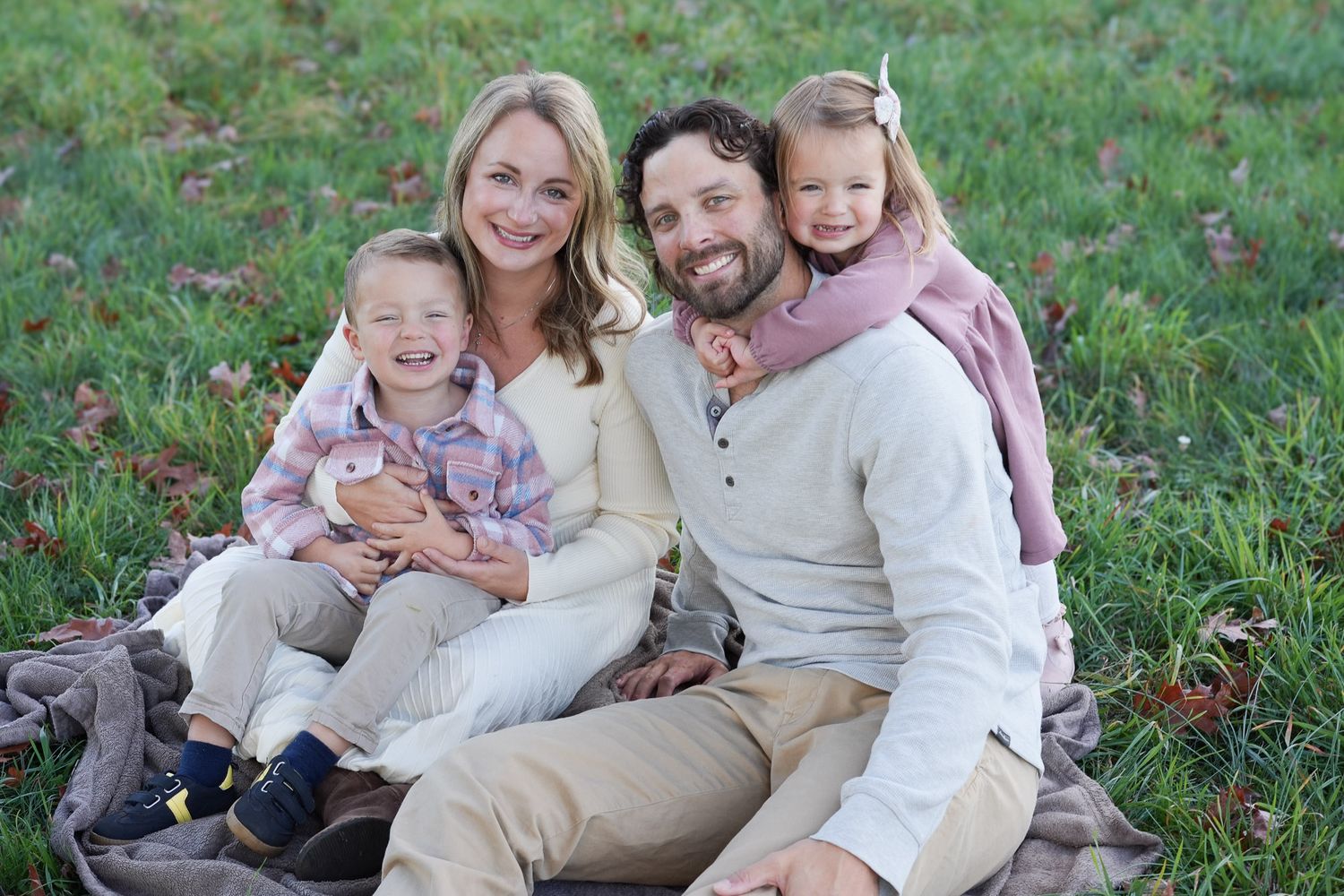 Happy family of four sitting on a blanket in a green field during an outdoor photo session.