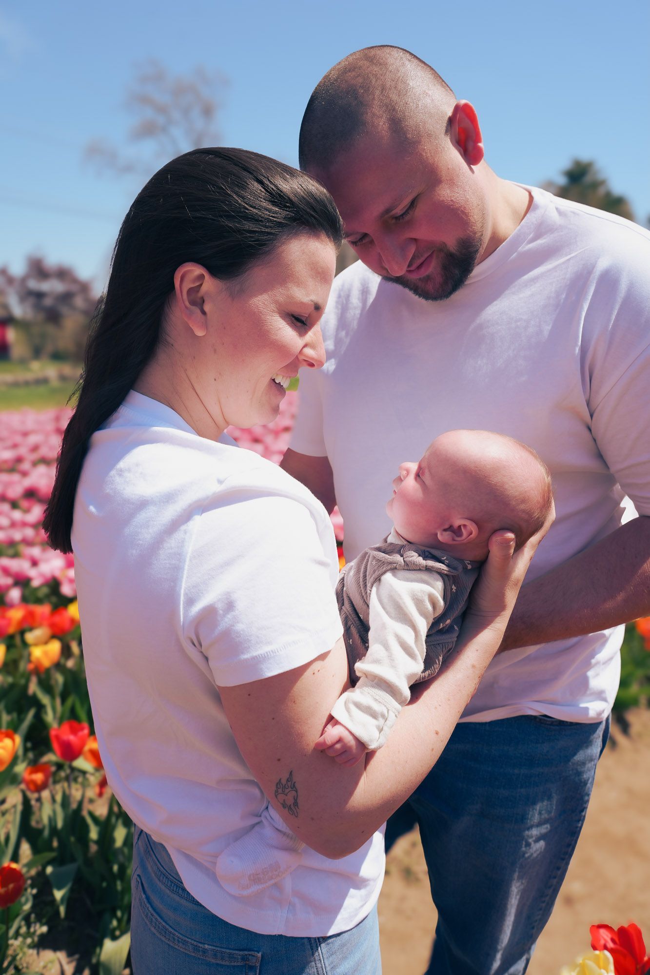 Loving parents in white shirts admiring their newborn baby in a colorful tulip field.