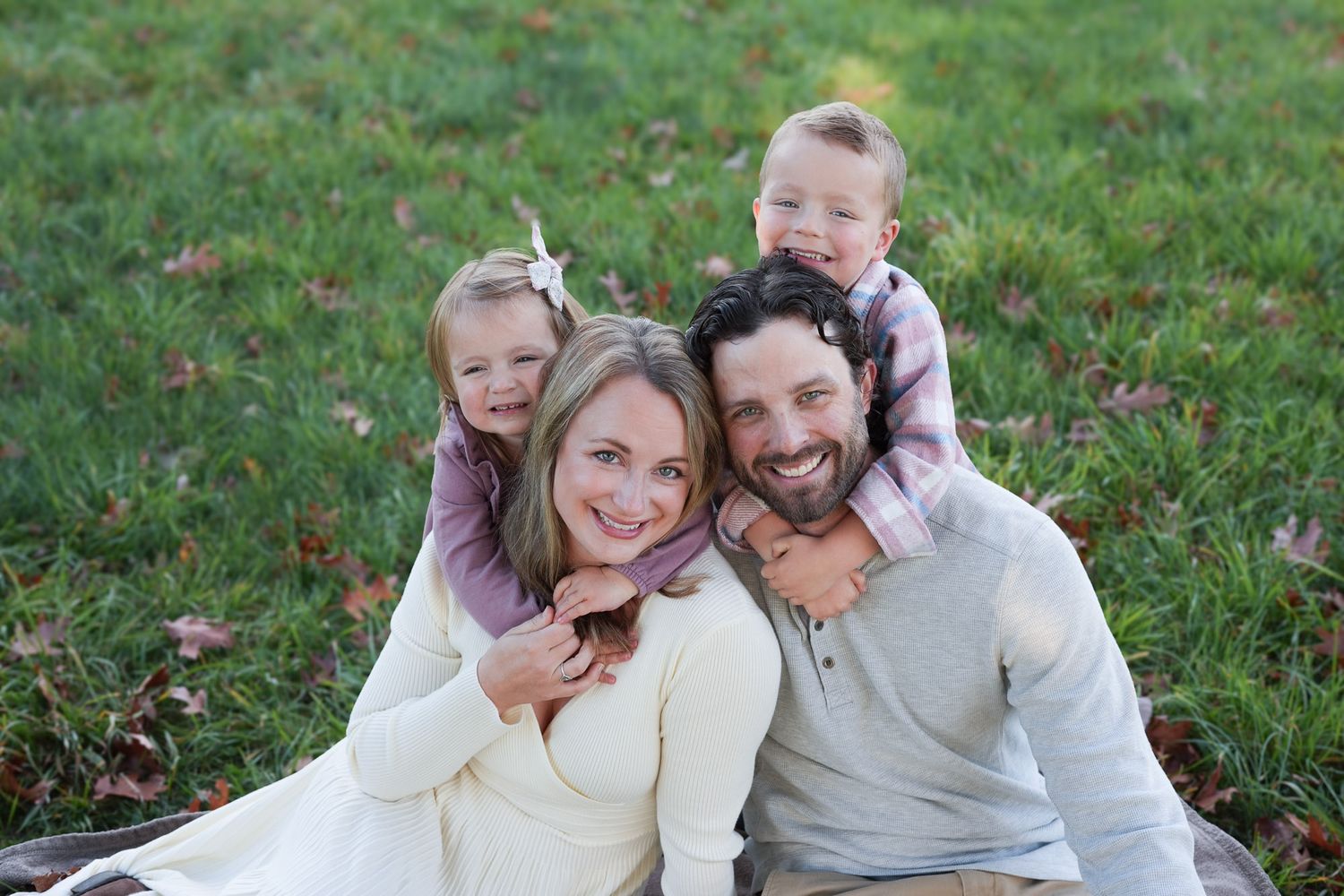 Smiling family of four posing closely together on a blanket in a green grassy outdoor setting.