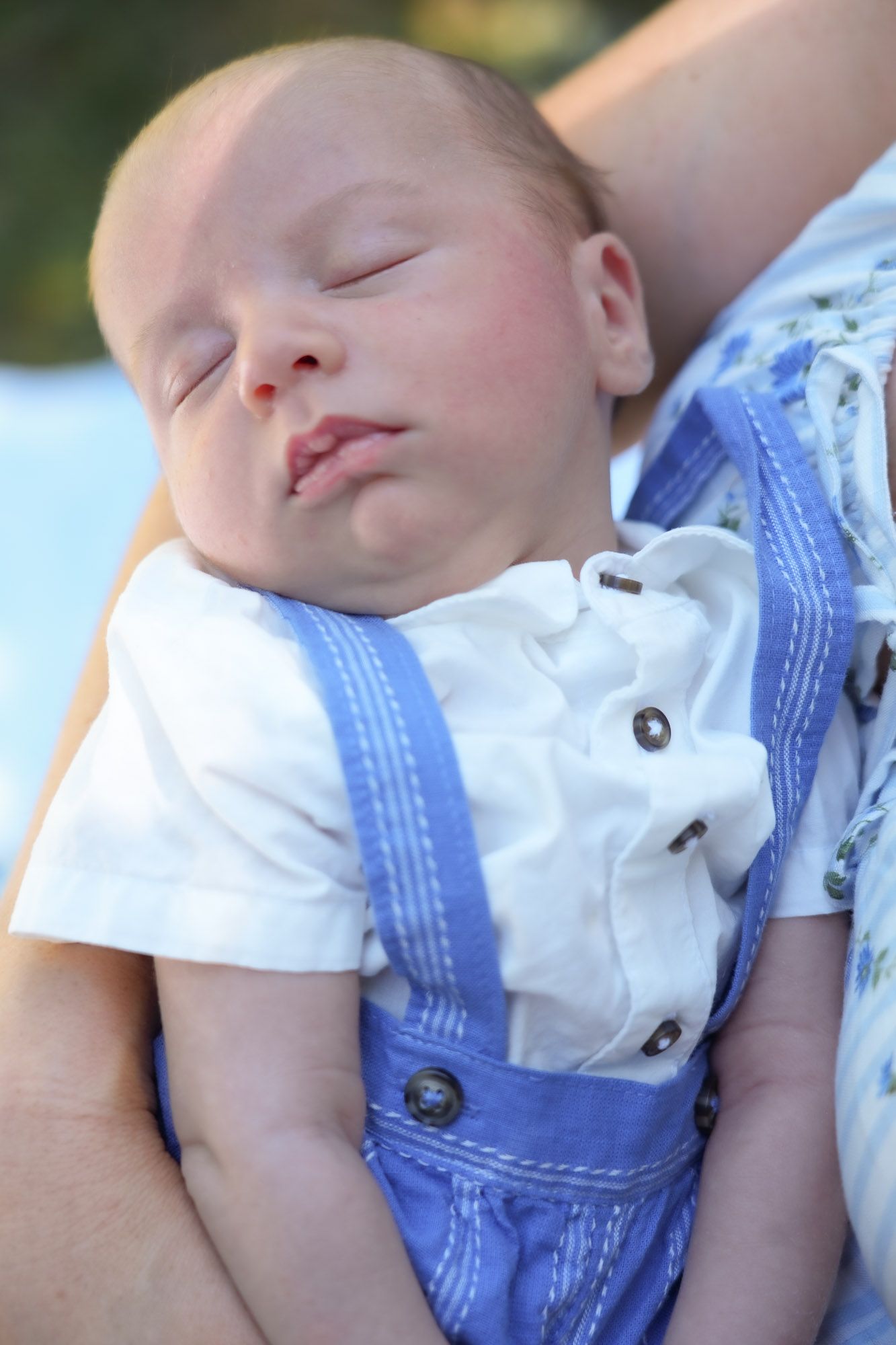 Close-up of peaceful sleeping newborn baby in white shirt and blue suspender romper.