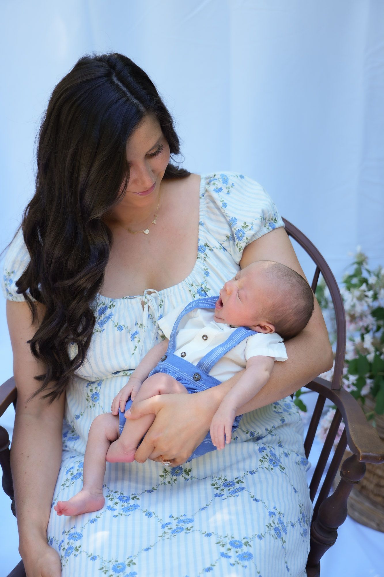 New mother gazing lovingly at her newborn baby in blue overalls.