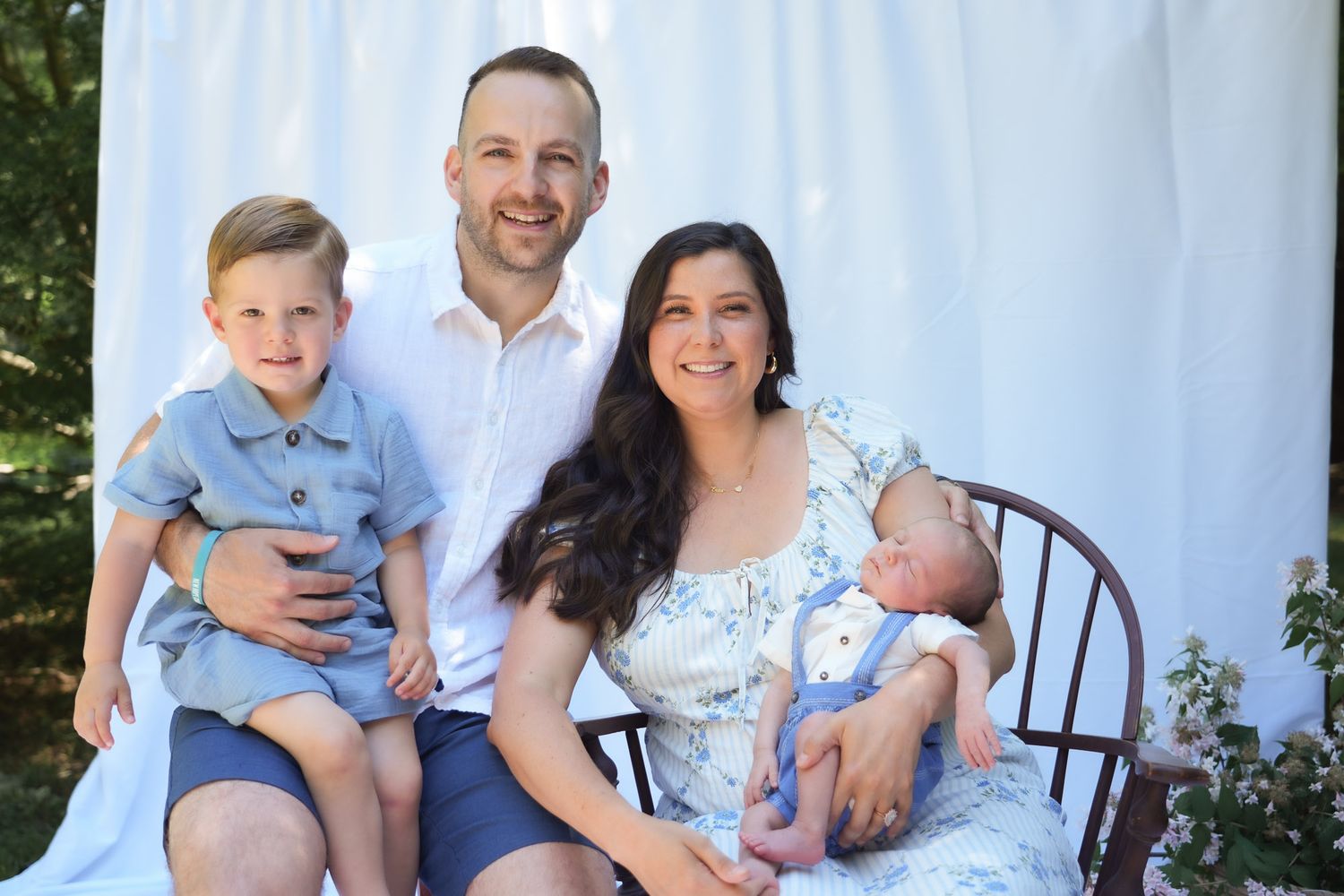 Happy family of four with toddler and newborn posing for outdoor portrait.