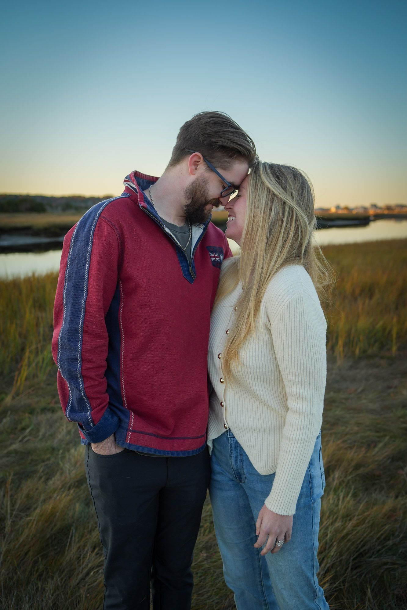 Romantic couple leaning foreheads together in a grassy marsh field at sunset.