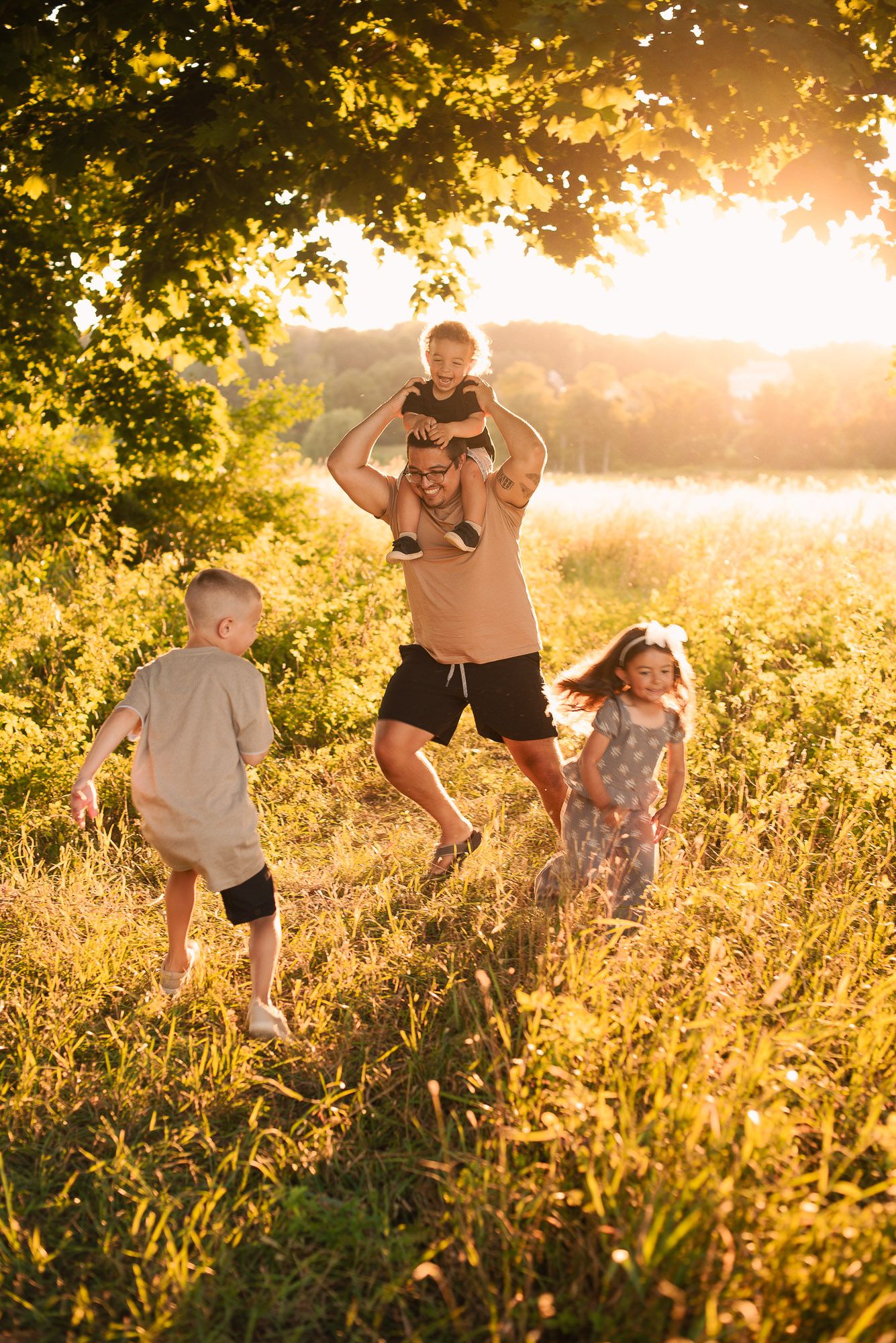 A joyful father plays with three young children in a sunlit meadow during golden hour.