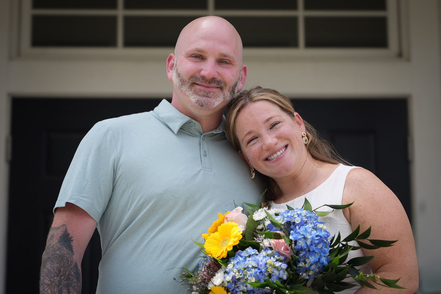 Joyful newlyweds smiling together, bride holding a vibrant blue and yellow floral bouquet.