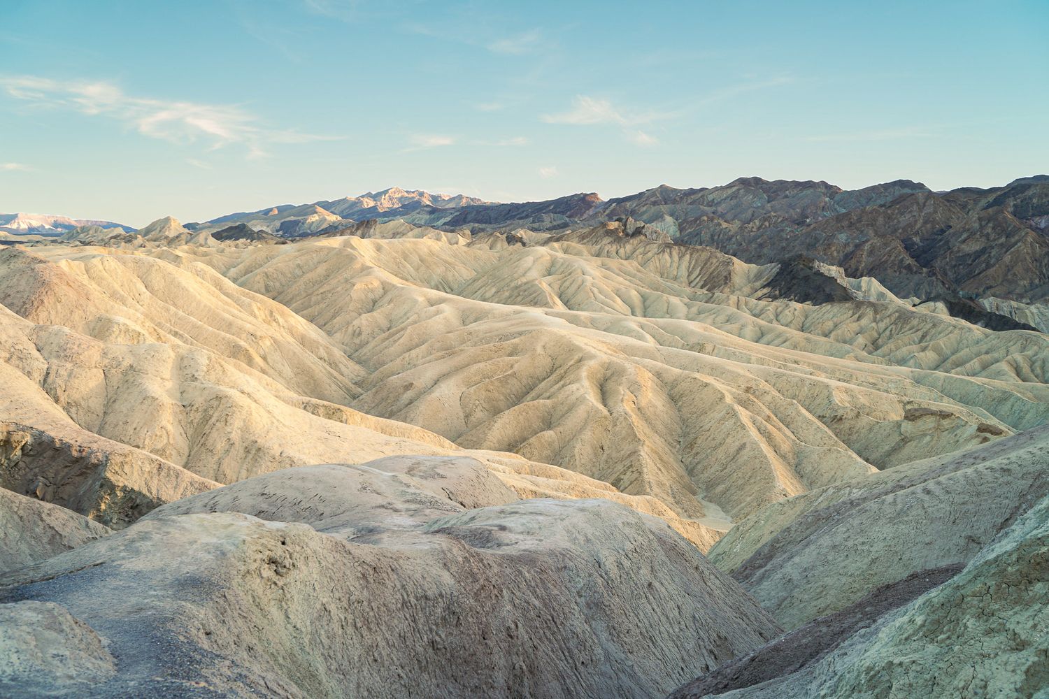 Zabriskie Point badlands in Death Valley showing eroded golden ridges and valleys under a pale blue sky.