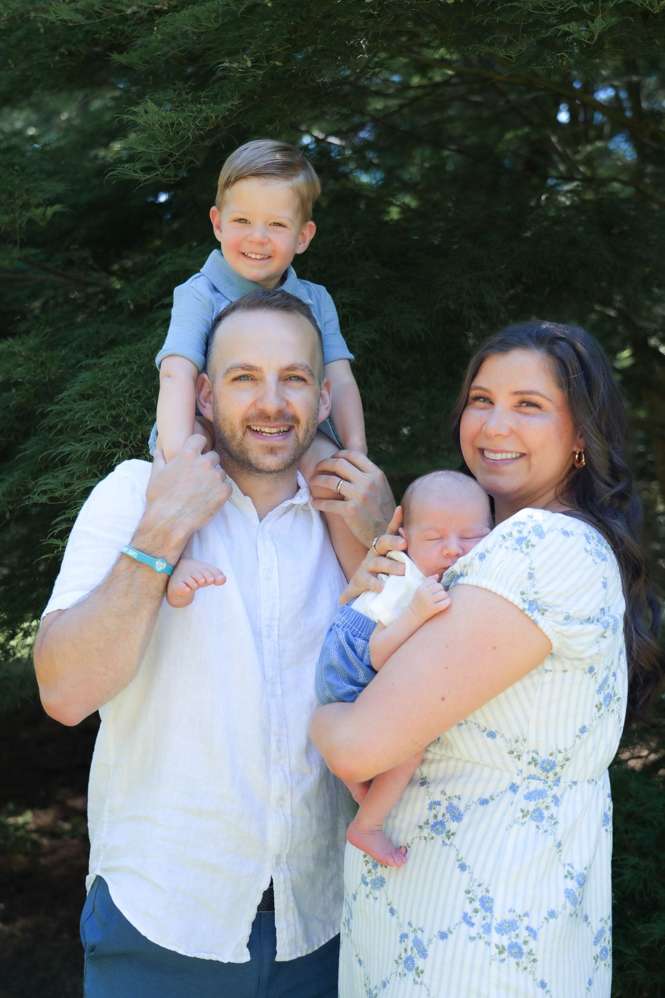 Happy family portrait with father, mother, newborn baby, and toddler son outdoors.